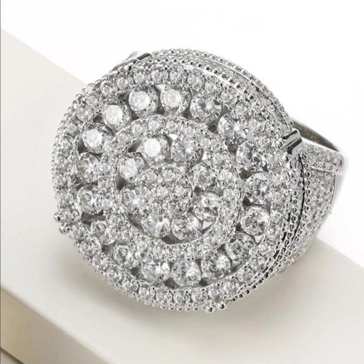 Anillo plateado de diseño circular con piedras brillantes y detalles tipo halo.