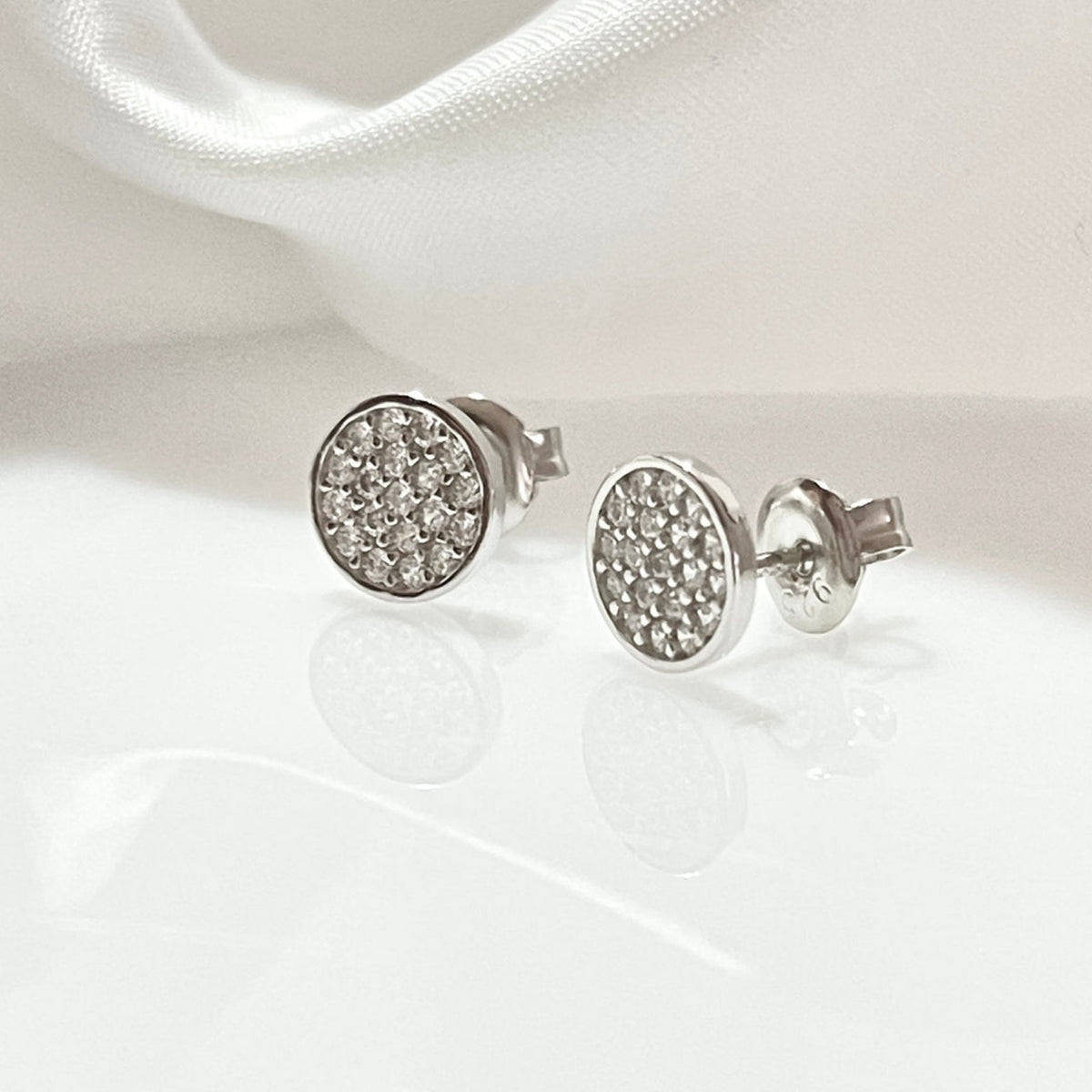 Aretes redondos plateados con diseño de piedras brillantes.