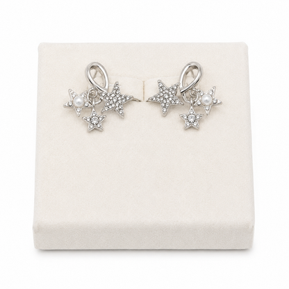 Aretes colgantes con diseño de estrellas plateadas y perlas decorativas.