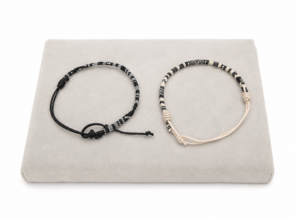 Set de 2 pulseras ajustables en negro y beige con diseño tejido estampado.