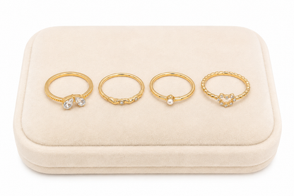 Set de 4 anillos dorados con detalles brillantes, corazón y perla.