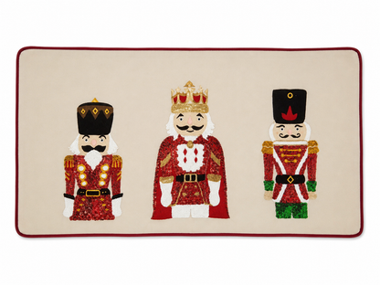 Camino de mesa navideño beige con tres cascanueces bordados y borde rojo.