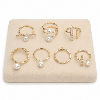 Set de 7 anillos dorados con diseños variados y detalles perlados.