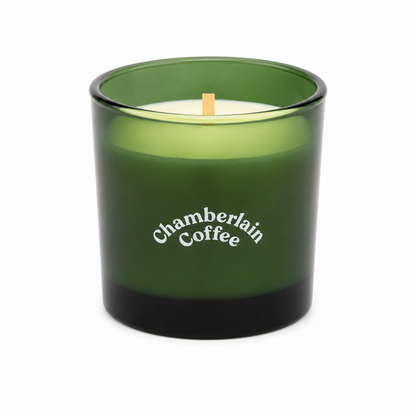 Vela decorativa aromática en recipiente de vidrio verde con mecha de madera.