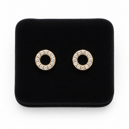 Aretes de botón circulares dorados con aro de piedras transparentes.