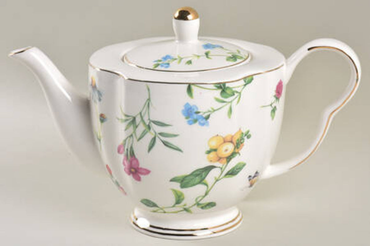Tetera de porcelana blanca con diseño floral y detalles dorados.