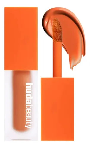 Huda Beauty en Color peach, reconocido por su frasco cuadrado transparente con tapa naranja.