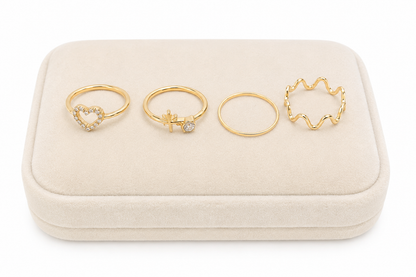 Set de 4 anillos dorados con diseños de corazón, cruz, aro liso y ondas.