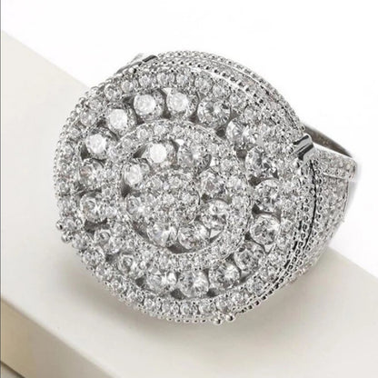 Anillo plateado de diseño circular con piedras brillantes y detalles tipo halo.