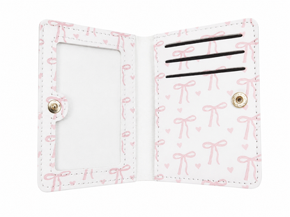 Billetera plegable con ventana para identificación y diseño de lazos en color blanco y rosa.