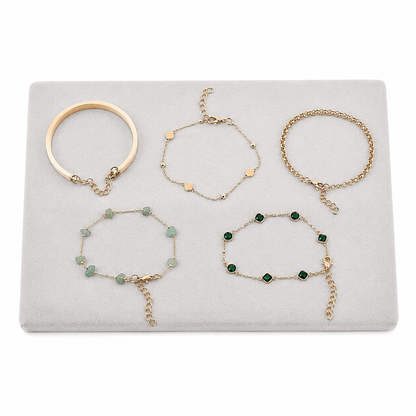 Set de 5 pulseras en tonos dorado, crema y verde con diseños variados.