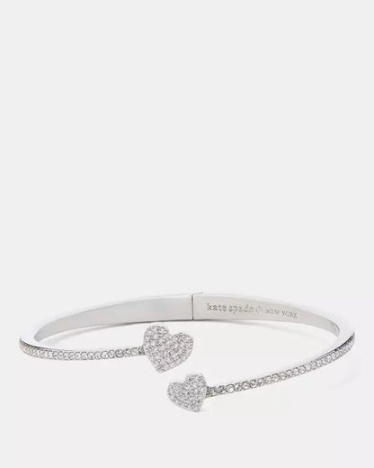 Brazalete plateado abierto con corazones y cristales decorativos.
