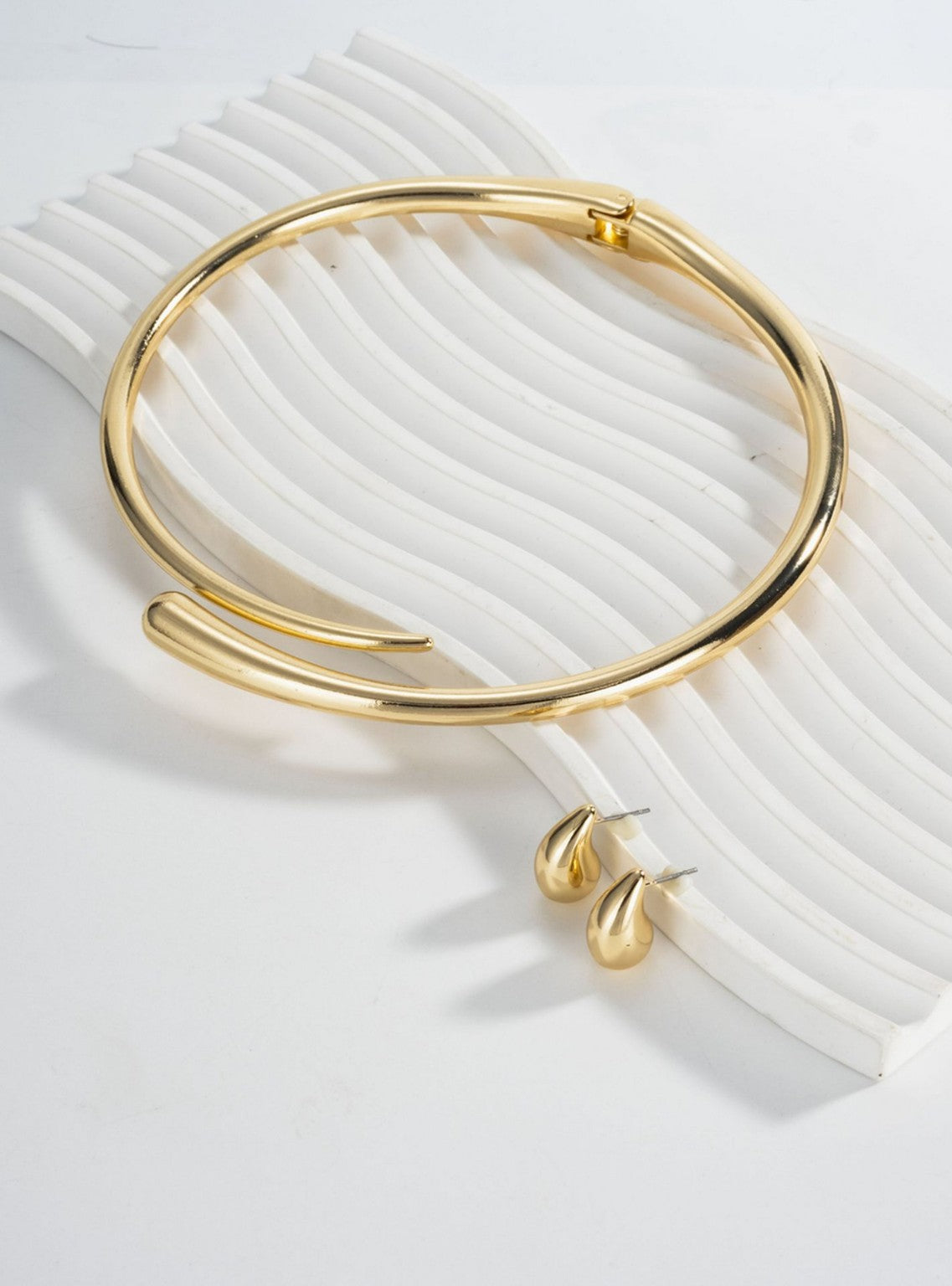 Conjunto de joyería dorada con collar rígido y aretes de gota.
