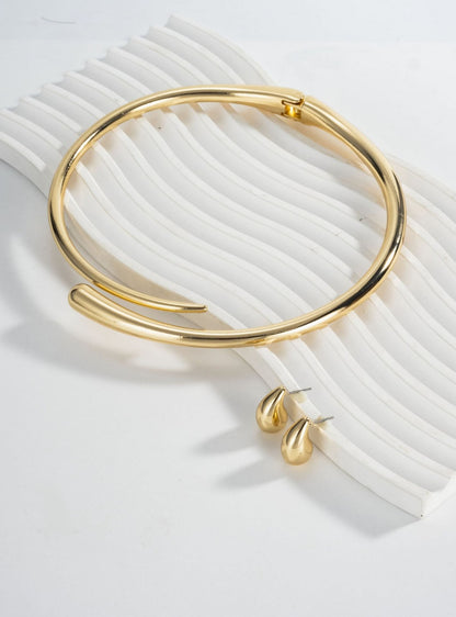 Conjunto de joyería dorada con collar rígido y aretes de gota.