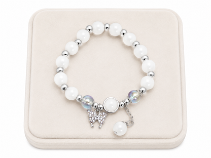 Pulsera elástica con cuentas blancas, dijes de mariposa y detalles en color plateado.