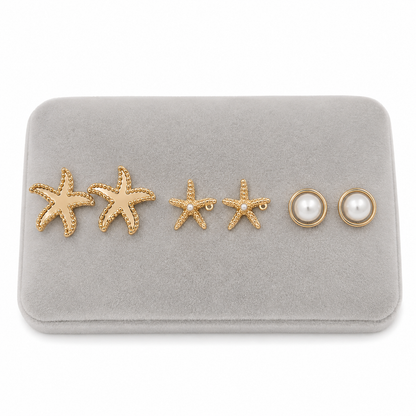 Set de tres pares de aretes dorados con estrellas de mar y perlas blancas.